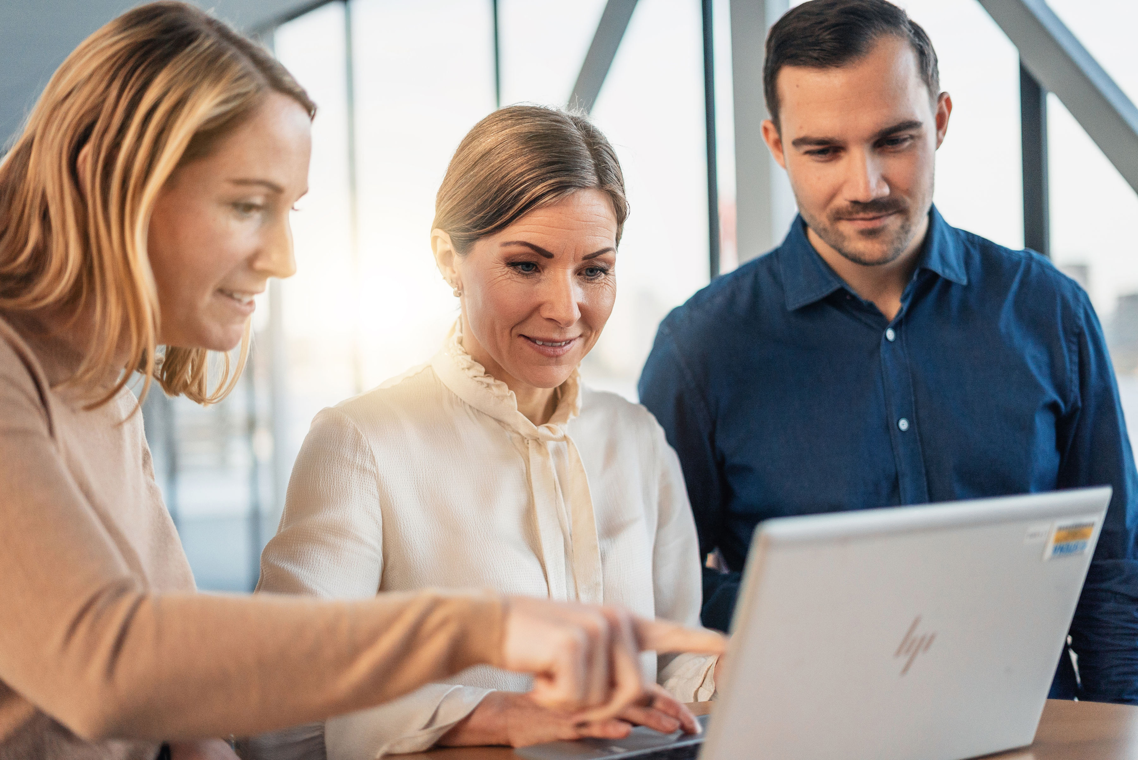 Kolme henkilöä, jotka seisovat kannettavan tietokoneen äärellä