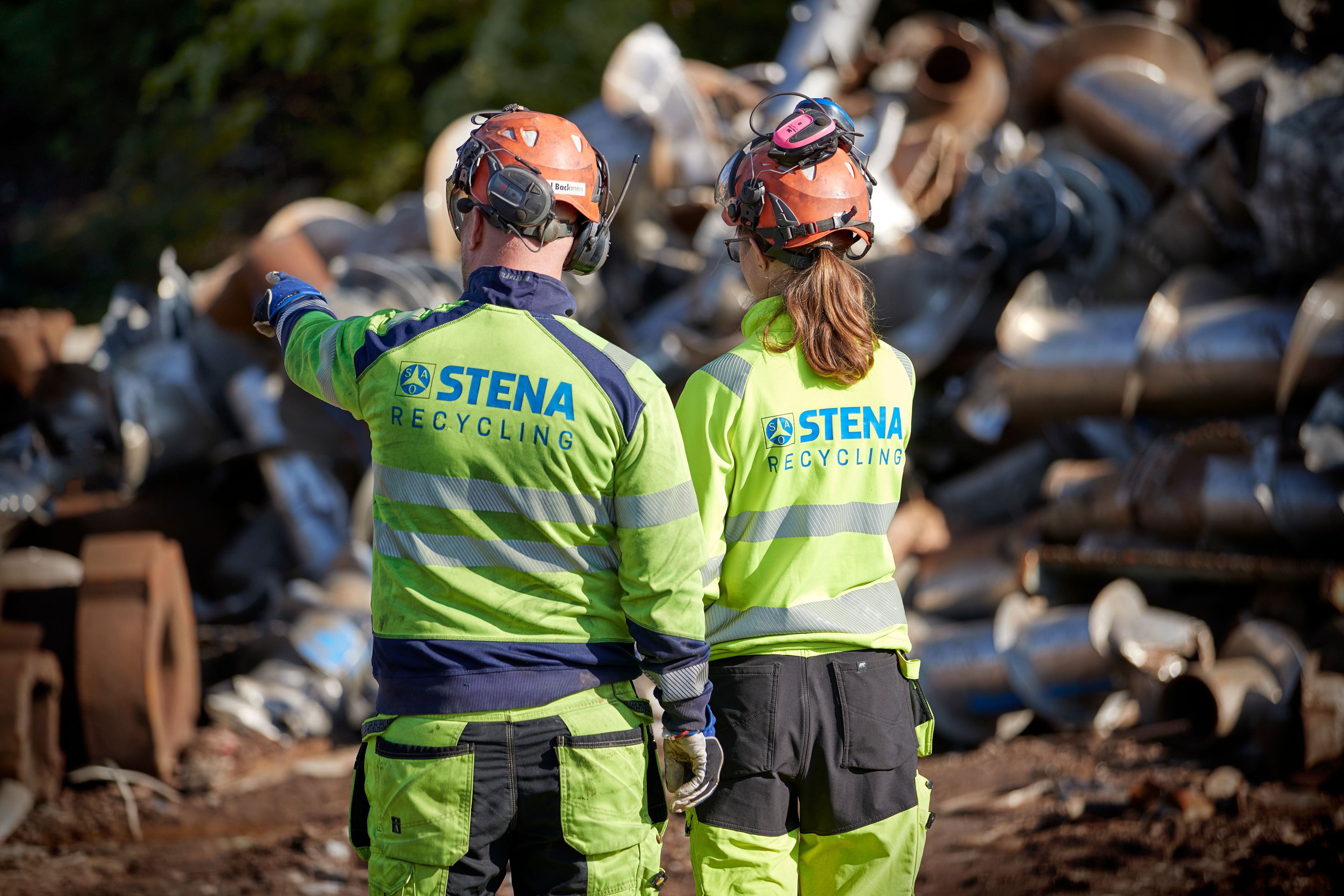 Two Stena Recycling employees in protective, hi-vis gear look at scrap