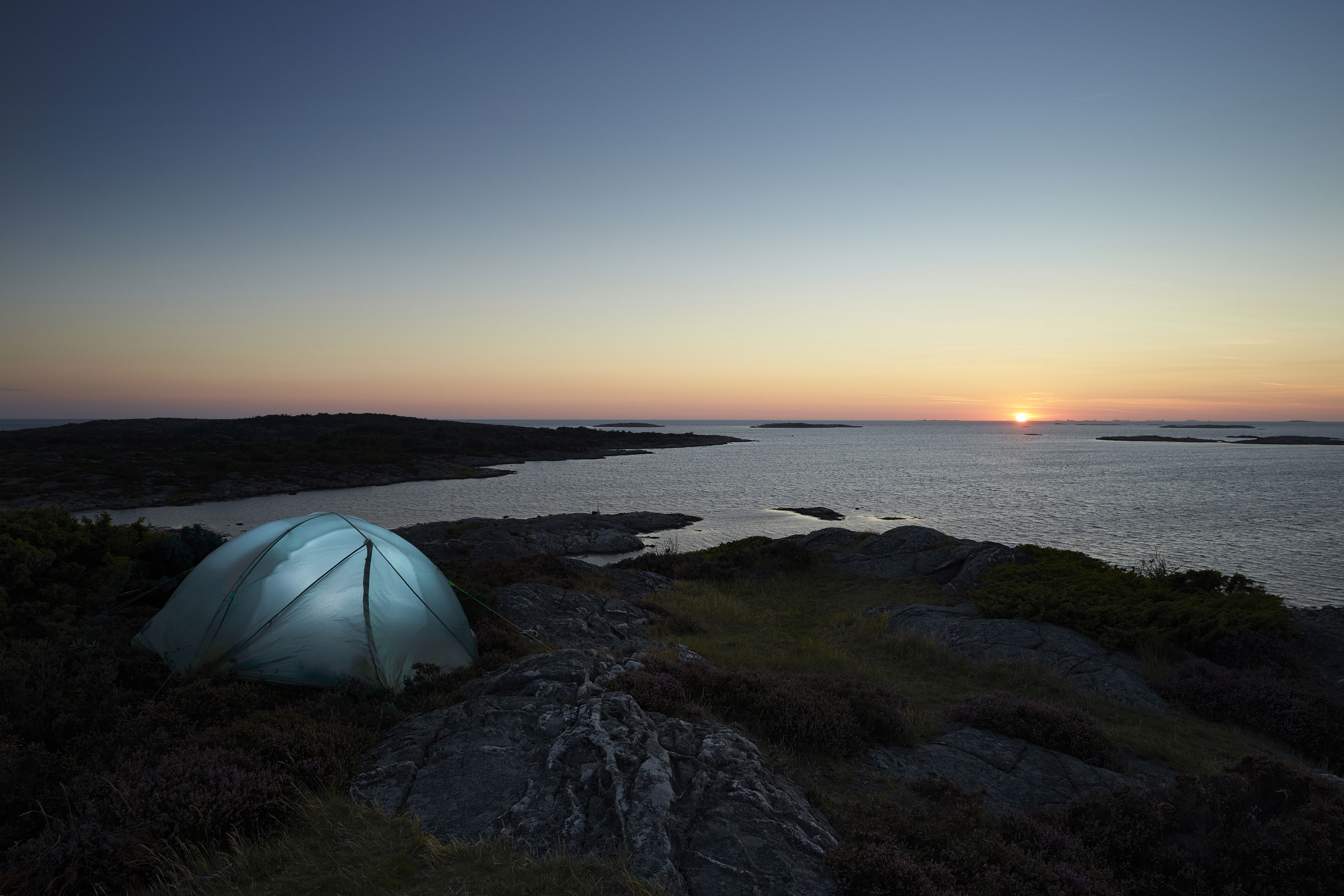 A small tent pitched on the Swedish west coast is illuminated as darkness falls.