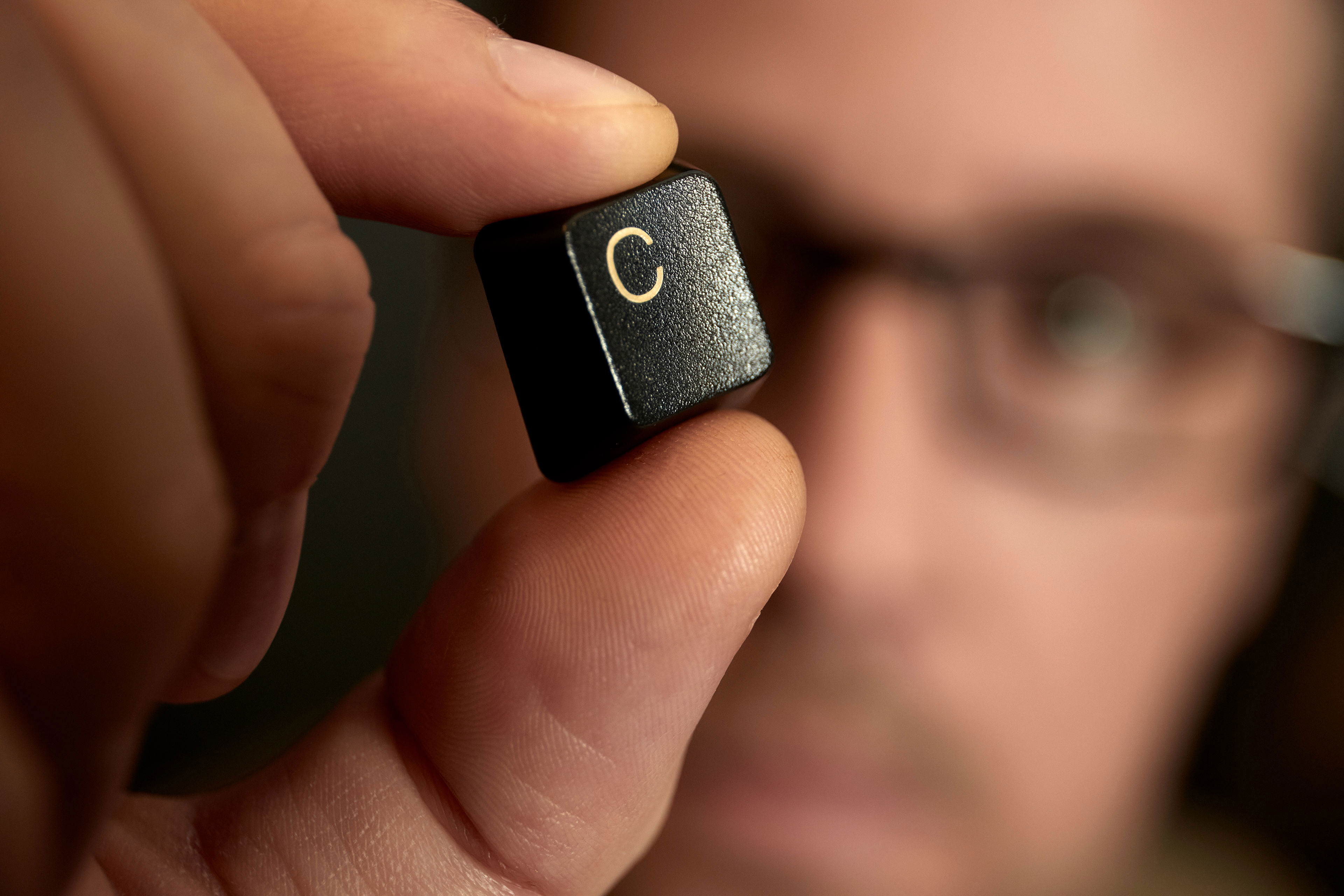 Close-up of a hand holding a keyboard key with the capital letter 'C' printed on it.