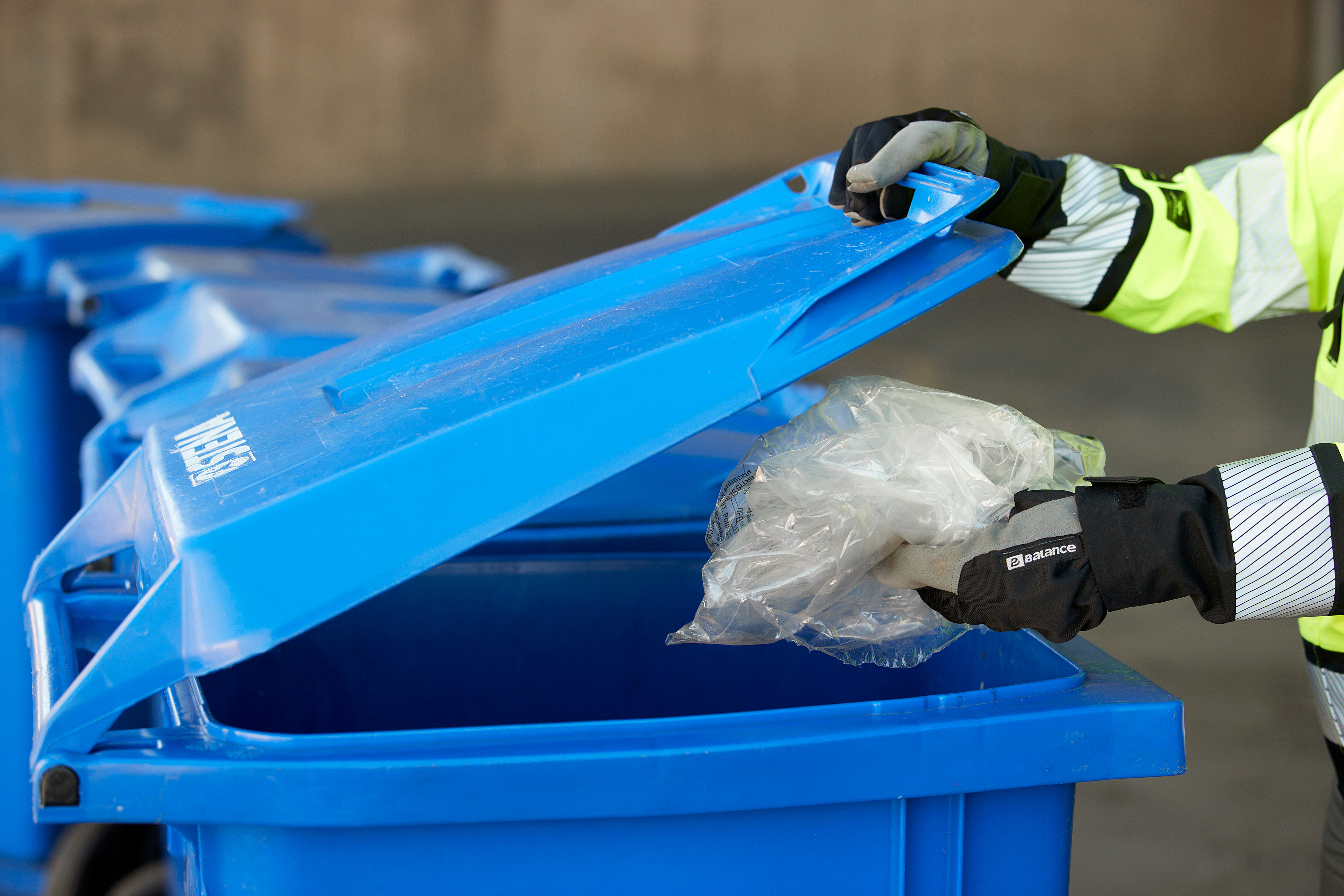 Närbild av en Stena Recycling anställd som lägger plast i ett återvinningskärl