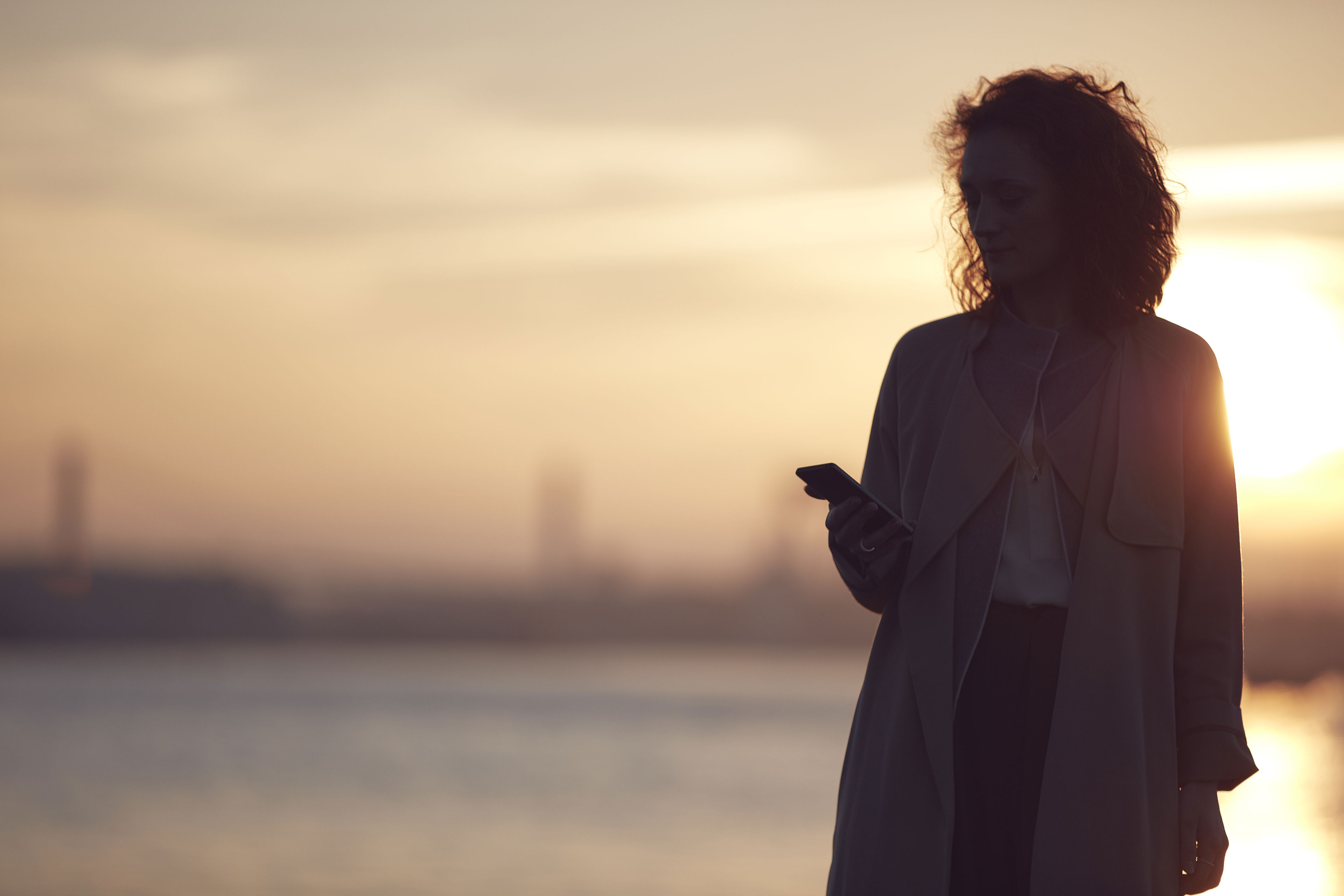 A woman looking at her phone in Gothenburg at sunset.
