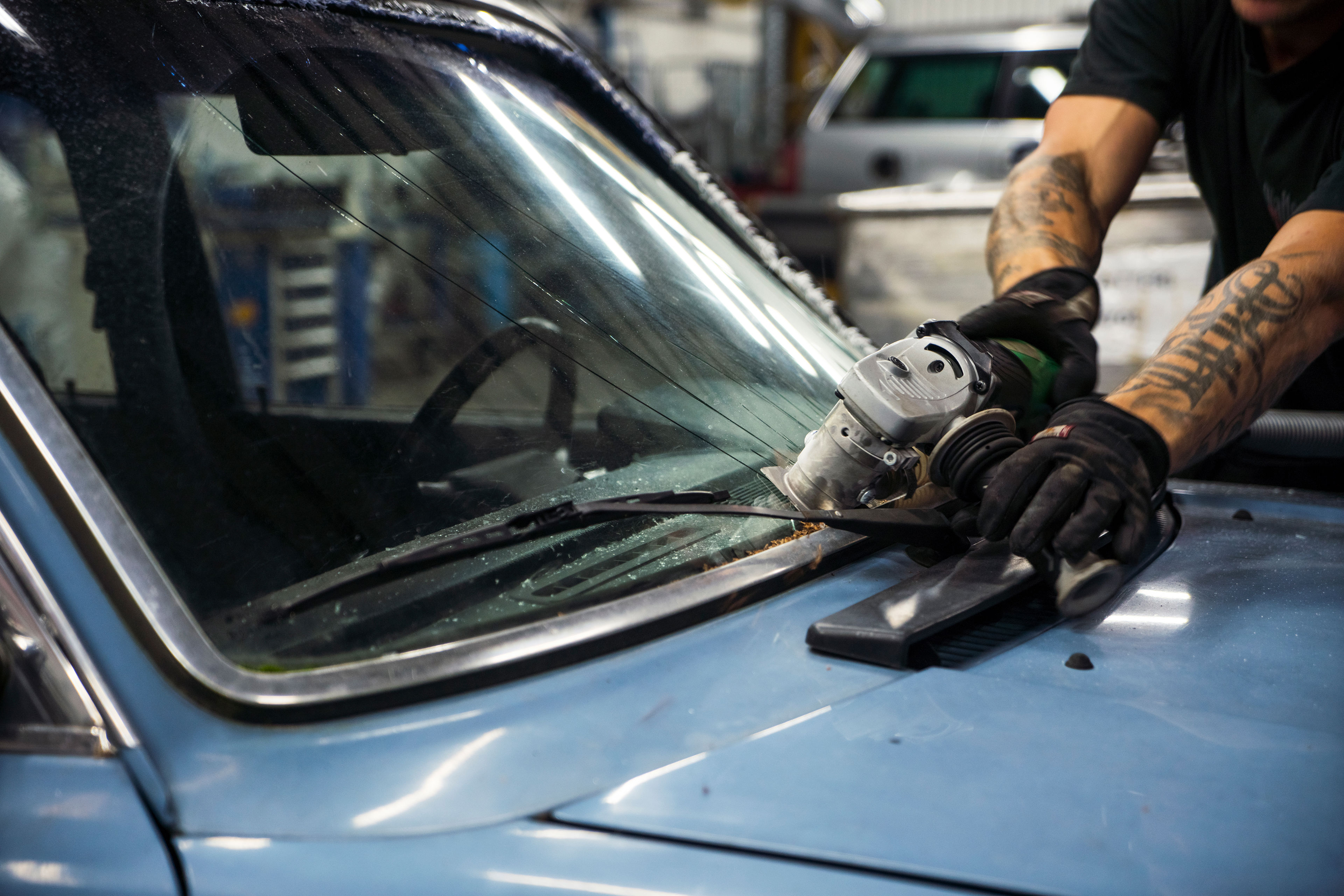 Close-up of a cracked windscreen being disassembled from a scrap car by using a handheld machine