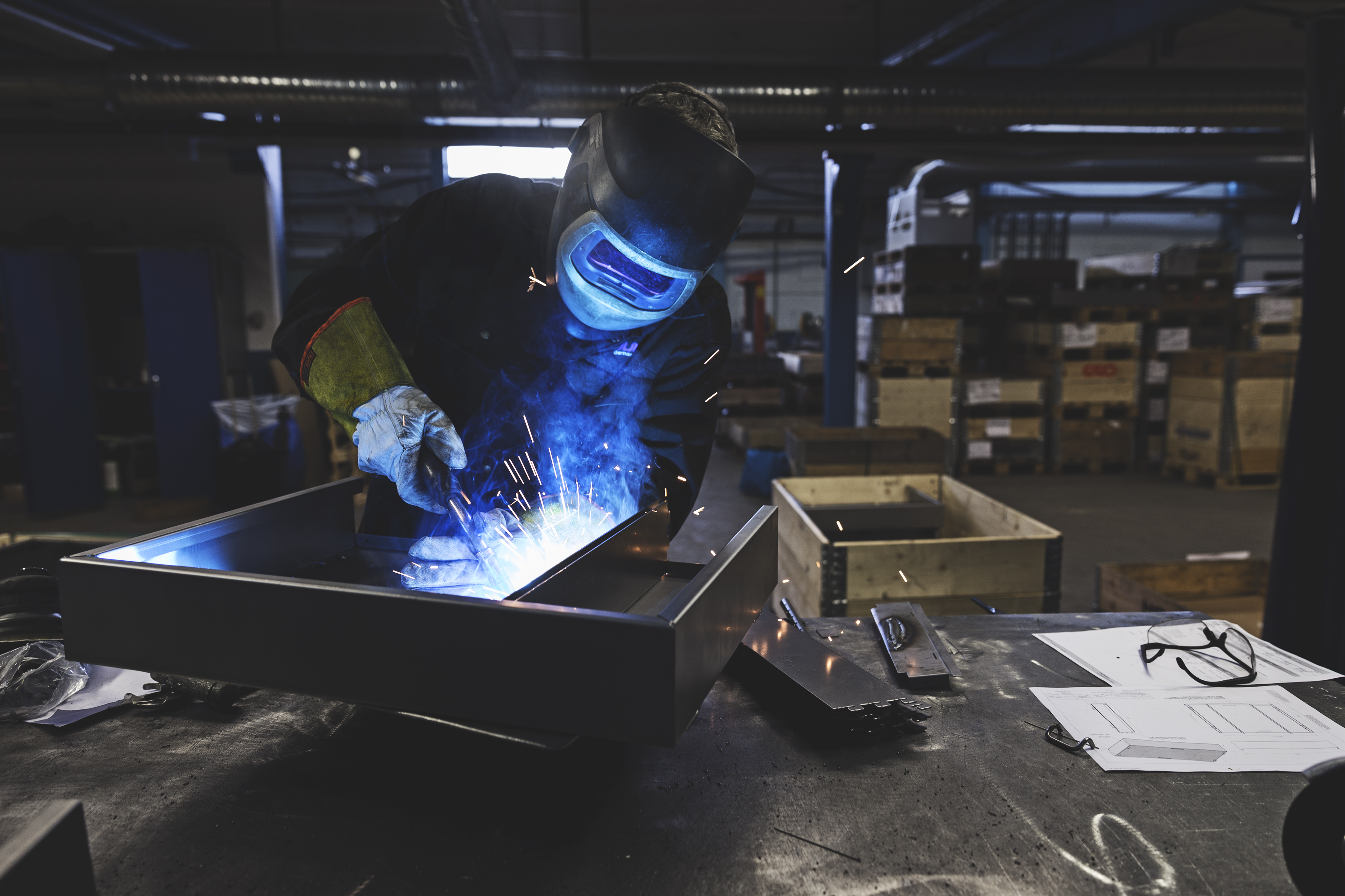 Pracownik używający środków ochrony indywidualnej spawa kawałek metalu w środowisku produkcyjnym.