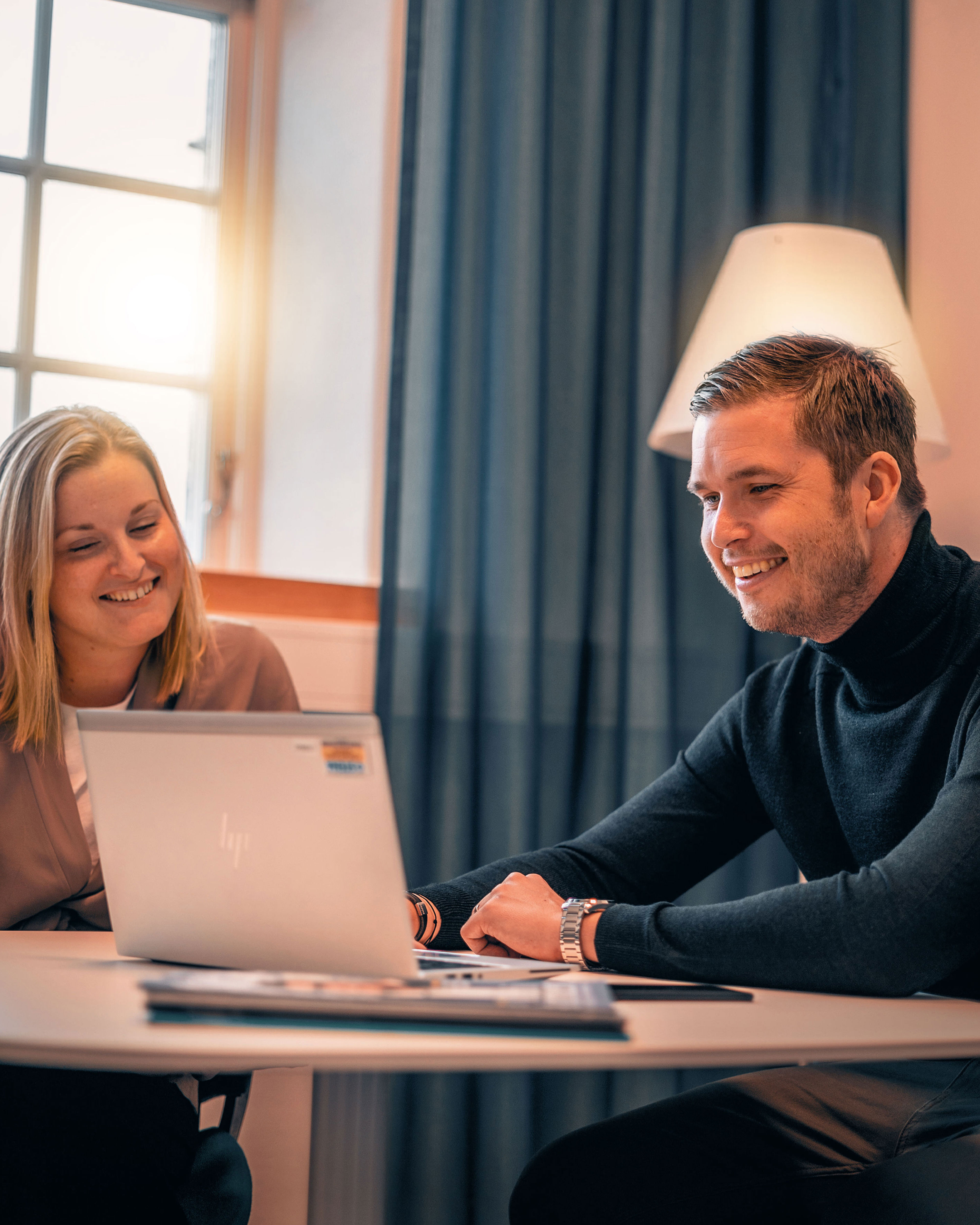 Cropped close-up image of a laptop on an office desk with the user’s forearm sleeves visible behind it